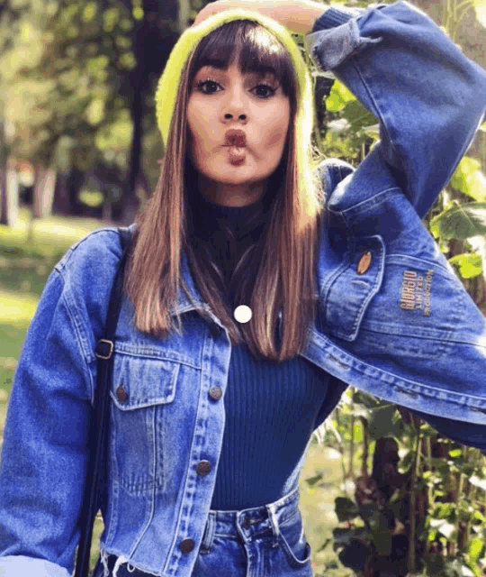 a woman wearing a denim jacket and a yellow beanie makes a face