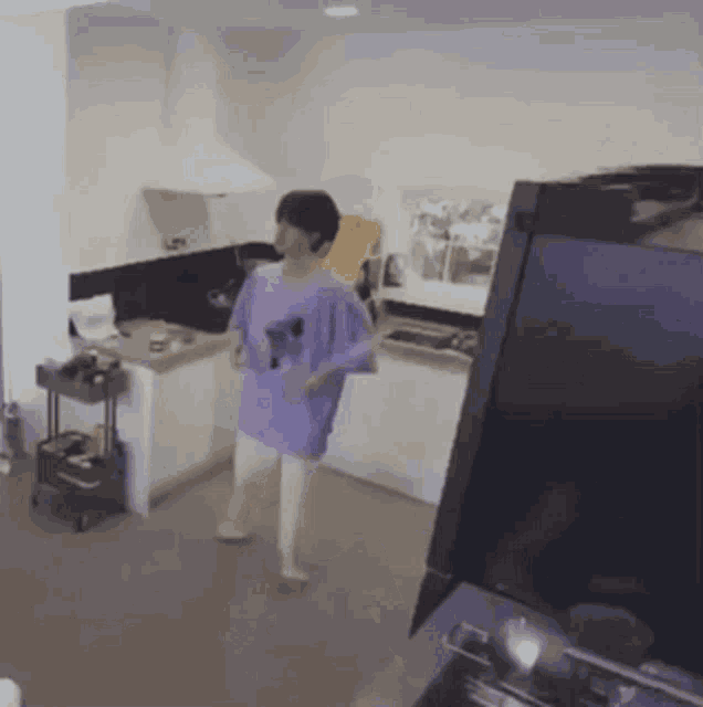 a man in a purple shirt is standing in a kitchen next to a laptop .