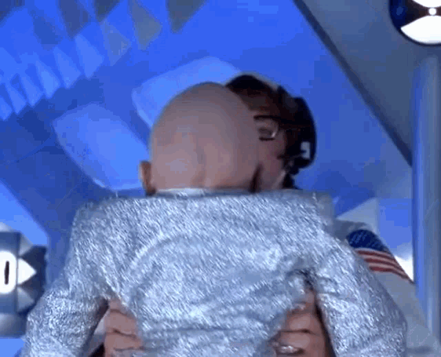 a man with a bald head is being held by another man in a silver suit .