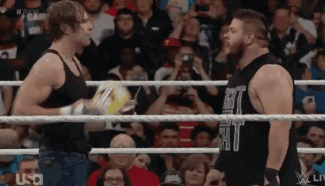 two wrestlers are standing in a wrestling ring talking to each other in front of a crowd .