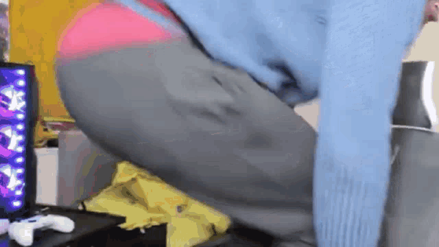 a person in a blue sweater is kneeling down on a couch with a video game controller in the background .