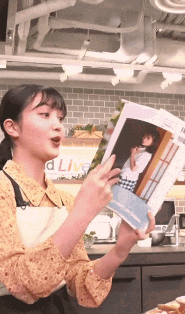 a woman in an apron is reading a book in front of a sign that says d live