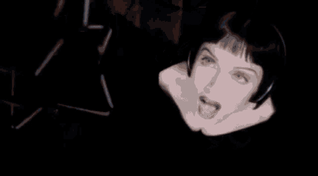 a silhouette of a person stands in front of a microphone in a dark room behind two reels of tape
