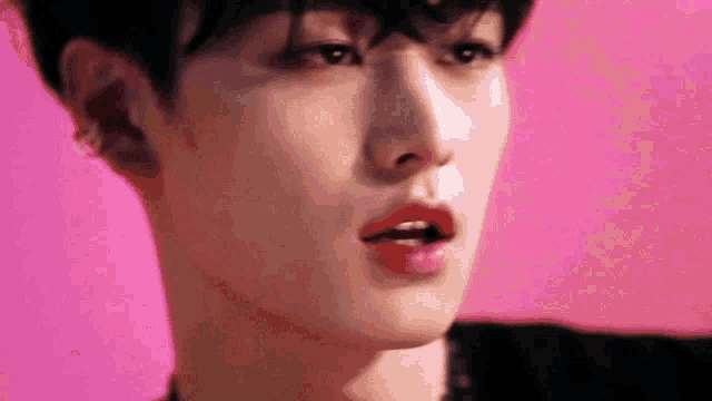 a close up of a young man 's face with a pink background and red lips .