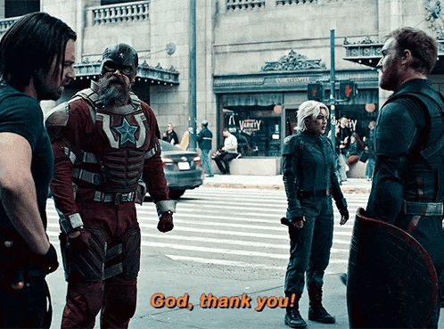 a group of superheros are standing on a street and one of them is saying god thank you