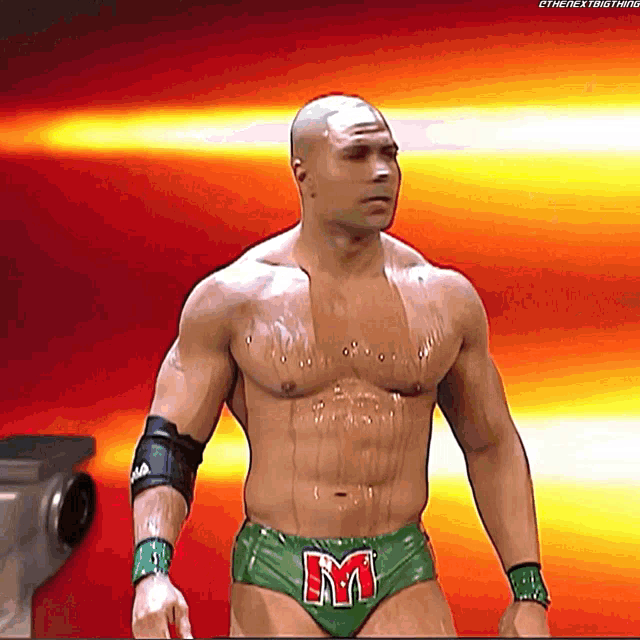 a shirtless wrestler in green underwear with the letter m on his belt
