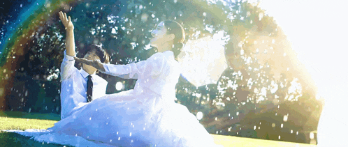 a bride and groom are sitting in the grass with their arms in the air