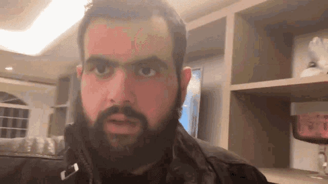 a man with a beard is standing in front of a shelf