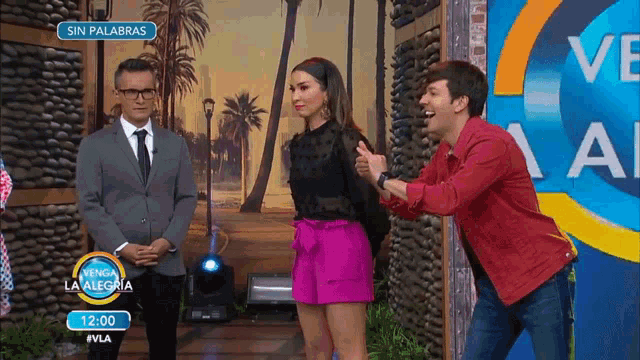 a man in a suit stands next to a woman in pink shorts and a man in a red jacket