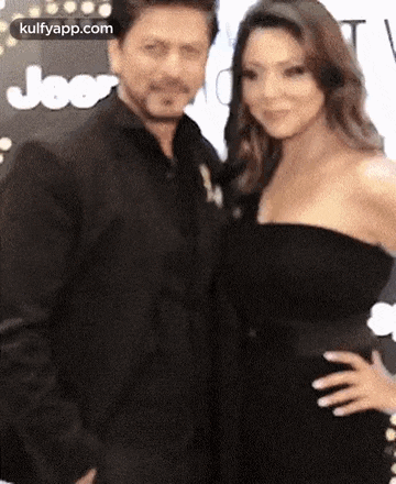 a man and a woman are posing for a picture together . the woman is wearing a strapless black dress .