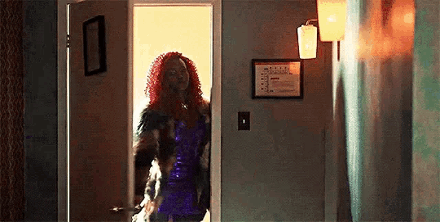 a woman in a purple dress and fur coat is standing in a doorway .