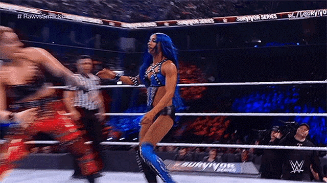 a woman with blue hair is dancing in a wrestling ring while a referee watches .