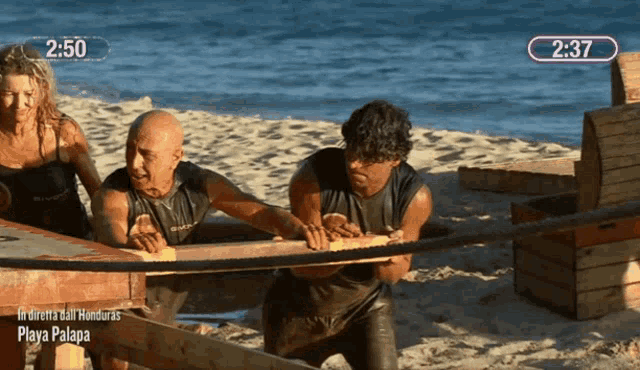 a group of people pulling a wooden plank on a beach with the time 2:37