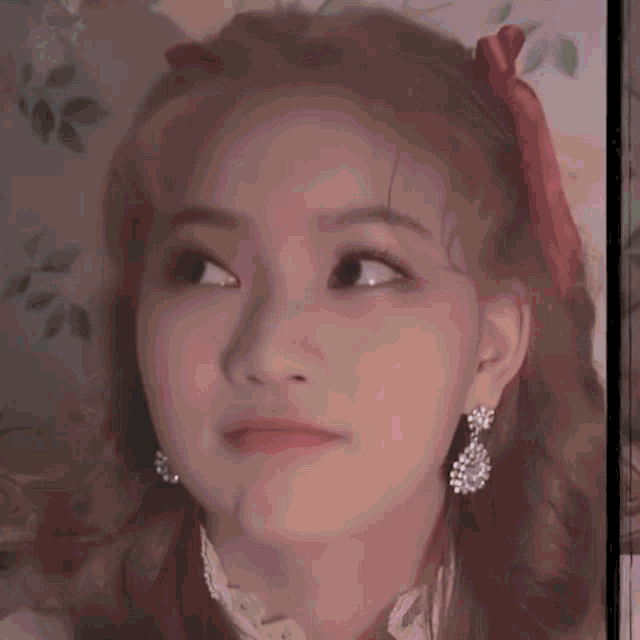 a close up of a woman 's face wearing earrings and a red bow in her hair .