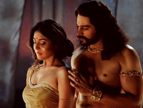 a man without a shirt is holding a woman 's shoulder