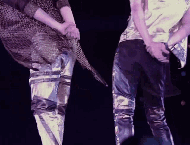two men are holding hands on a stage and one has a microphone in his hand