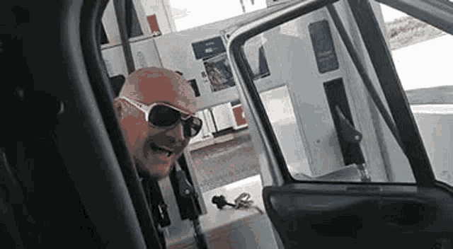 a man wearing sunglasses is standing in a car at a gas station .