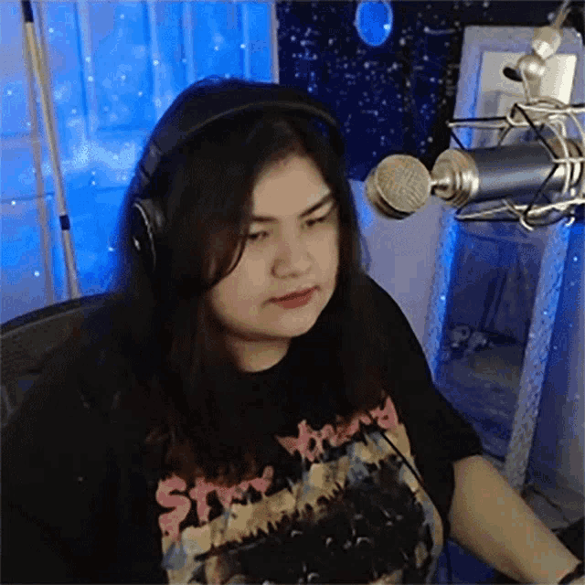 a woman wearing headphones is sitting in front of a microphone in a recording studio .