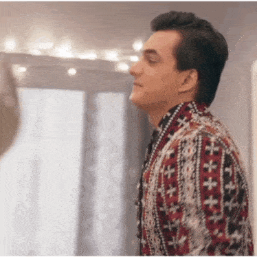 a man in a sweater is standing in front of a window and looking at something .