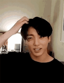 a young man in a black shirt is touching his hair and smiling
