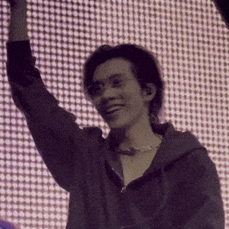 a man in a hoodie is smiling and raising his hand in the air