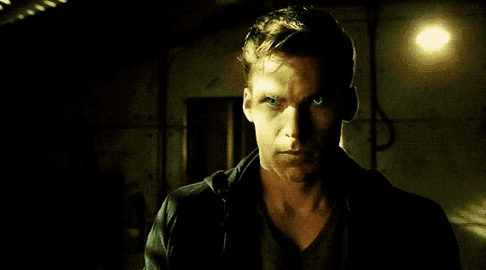 a close up of a man 's face in a dark room with a light behind him .
