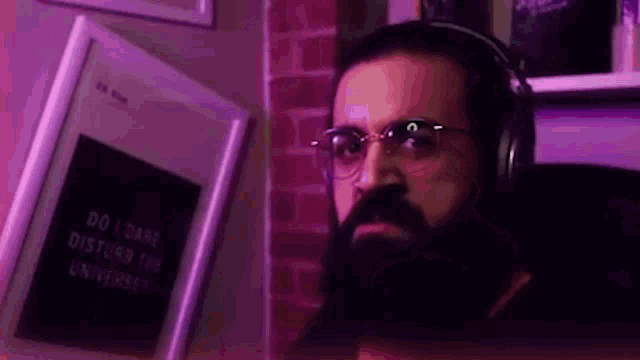 a man with a beard and headphones is sitting in front of a book that says `` do i dare disturb the universe ''