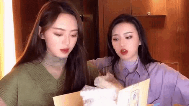 two young women are looking at a piece of paper together .