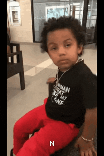 a young boy wearing a black shirt and red pants is sitting in a chair .
