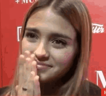 a close up of a woman 's face with her hands folded in front of a red wall .