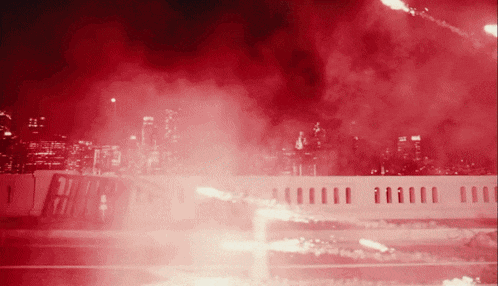 a red background with a white fence in the foreground and a city in the background