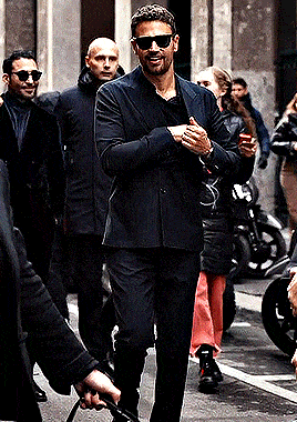 a man wearing sunglasses and a suit walks down a street