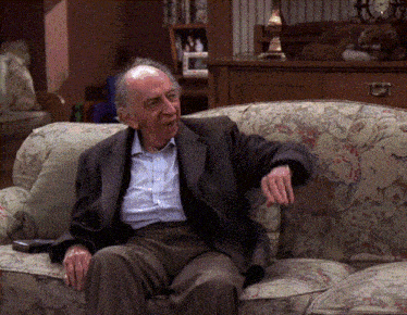 a man in a suit sits on a floral couch with his hand on his chin