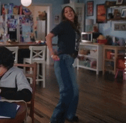 a woman is dancing in a living room with a child sitting at a table