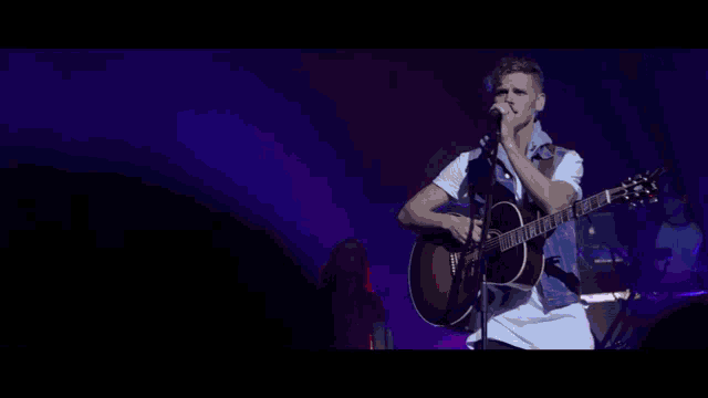 a man singing into a microphone while playing a guitar on stage