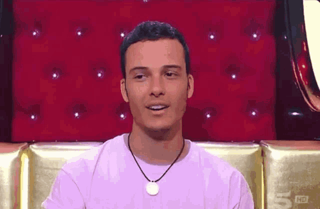 a man in a purple shirt is sitting in front of a red couch with the number 5 hd on it
