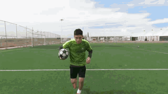 a man in a green shirt is running with a soccer ball on a field