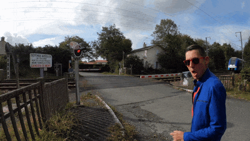 a man in a blue jacket stands in front of a railroad crossing with a sign that says " defense arcelor " on it