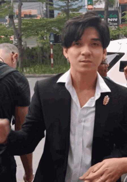 a man in a black suit and white shirt is walking down a street