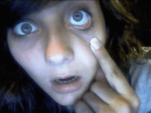 a close up of a woman 's face with a white nail polish on her finger