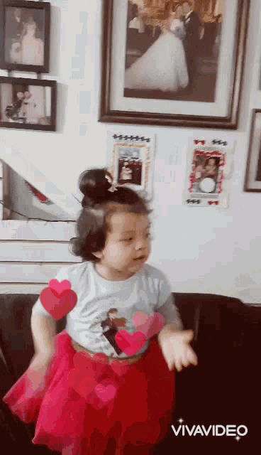 a little girl in a red skirt is dancing in front of a wall of pictures