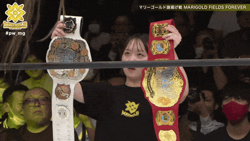 a woman in a black shirt with marigold fields forever on it is holding a wrestling belt