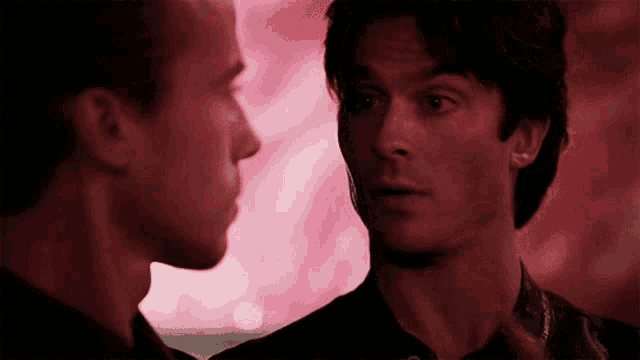 two men are looking at each other in front of a pink background