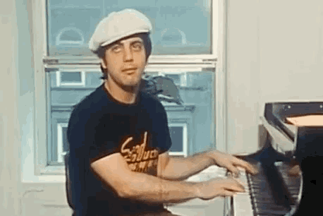 a man wearing a hat and a black shirt is playing the piano .