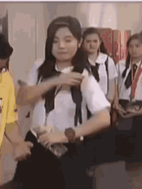 a girl in a school uniform is standing in a hallway with a group of students .
