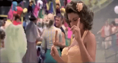 a woman in a yellow dress is standing in front of a crowd of people holding a lollipop .