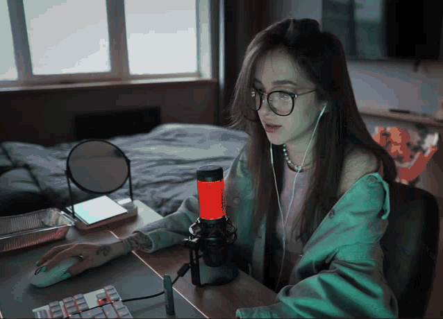 a woman wearing glasses is sitting at a desk with a microphone in front of her