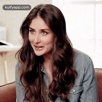 a woman in a denim jacket is sitting on a couch and smiling .