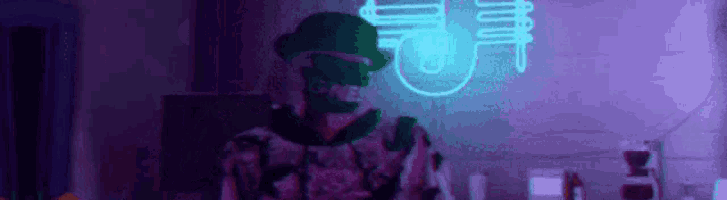 a man in a hat is standing in front of a neon sign in a room .