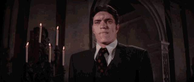 a man in a suit and tie is standing in front of candles and looking at the camera .